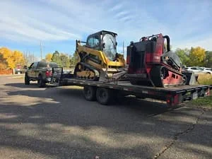 Flatbed trailer transporting compact track loader and landscaping equipment