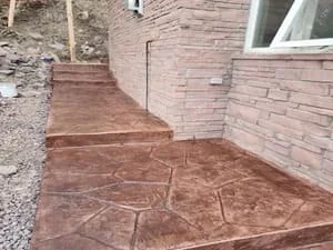 Stamped concrete patio with geometric stone pattern next to brick home