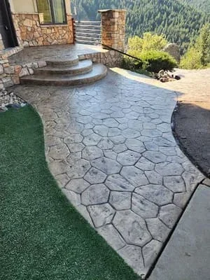 Stamped concrete patio with ashlar pattern, curved steps, and stone pillars overlooking mountains